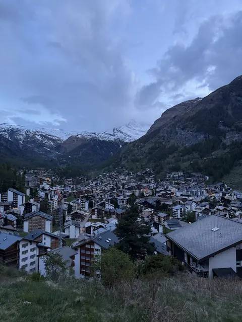 Chalet roofs and warm windows fill the valley beneath snowy mountains at dusk.