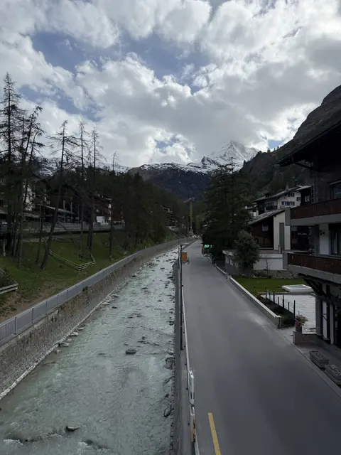 A pale glacial river runs between chalets toward a snowy peak.