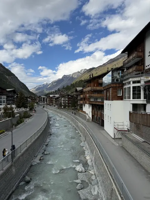 A river curves through the village beneath mountains and blue sky.