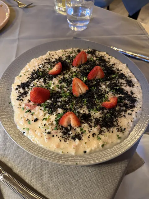 A creamy dish topped with strawberries, dark crumbs, and chopped herbs.