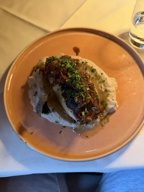 A browned entrée with onions and herbs rests on purée on an orange plate.
