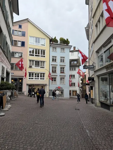 Swiss flags hang above a cobbled street lined with pastel buildings.