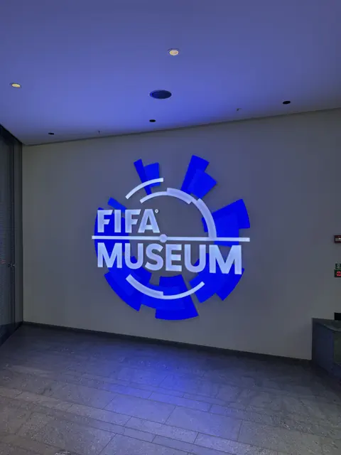 A blue illuminated FIFA Museum sign on an interior wall.